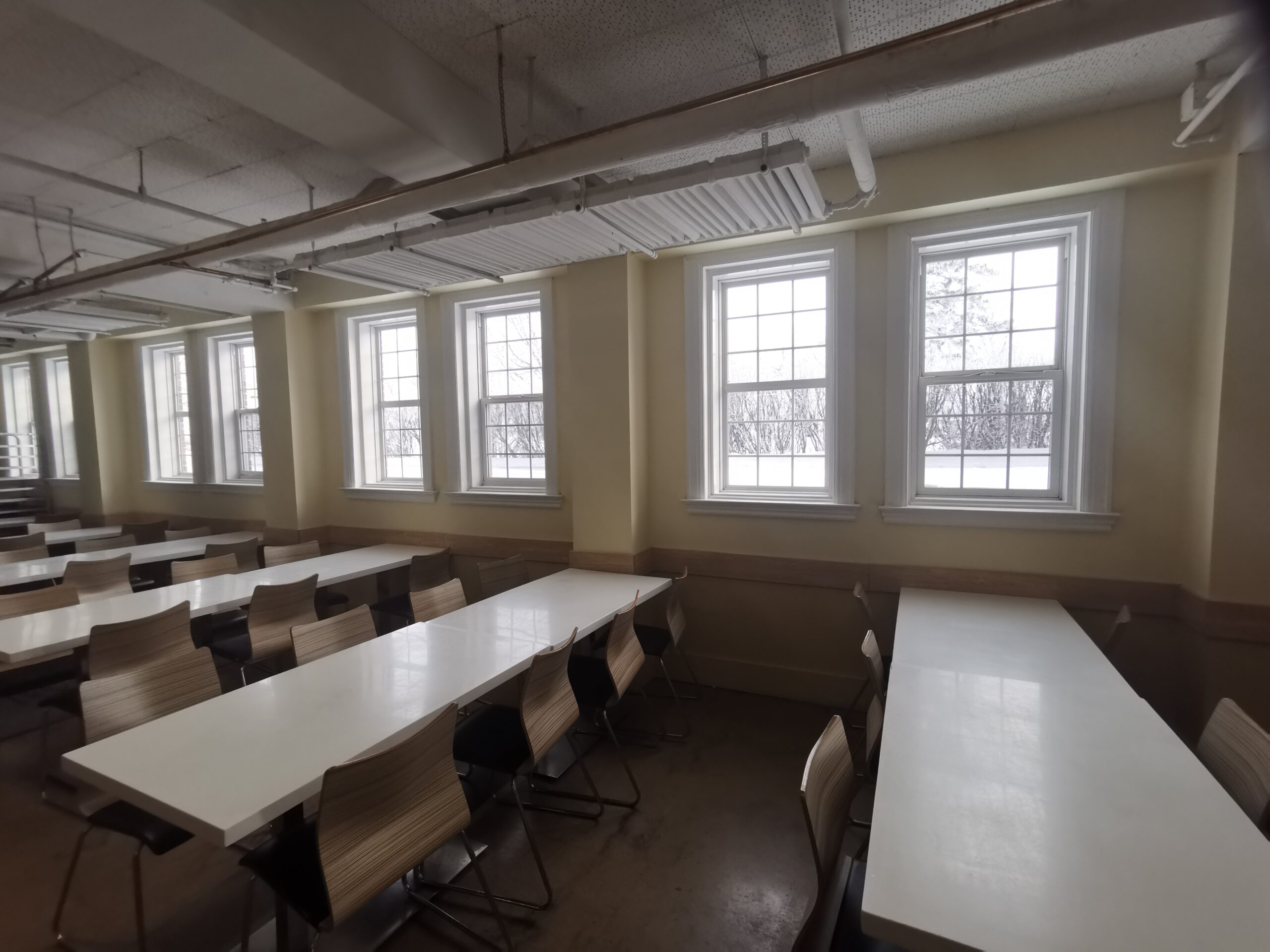 A spacious, well-lit classroom with large windows and rows of desks and chairs, ideal for students and educational activities.