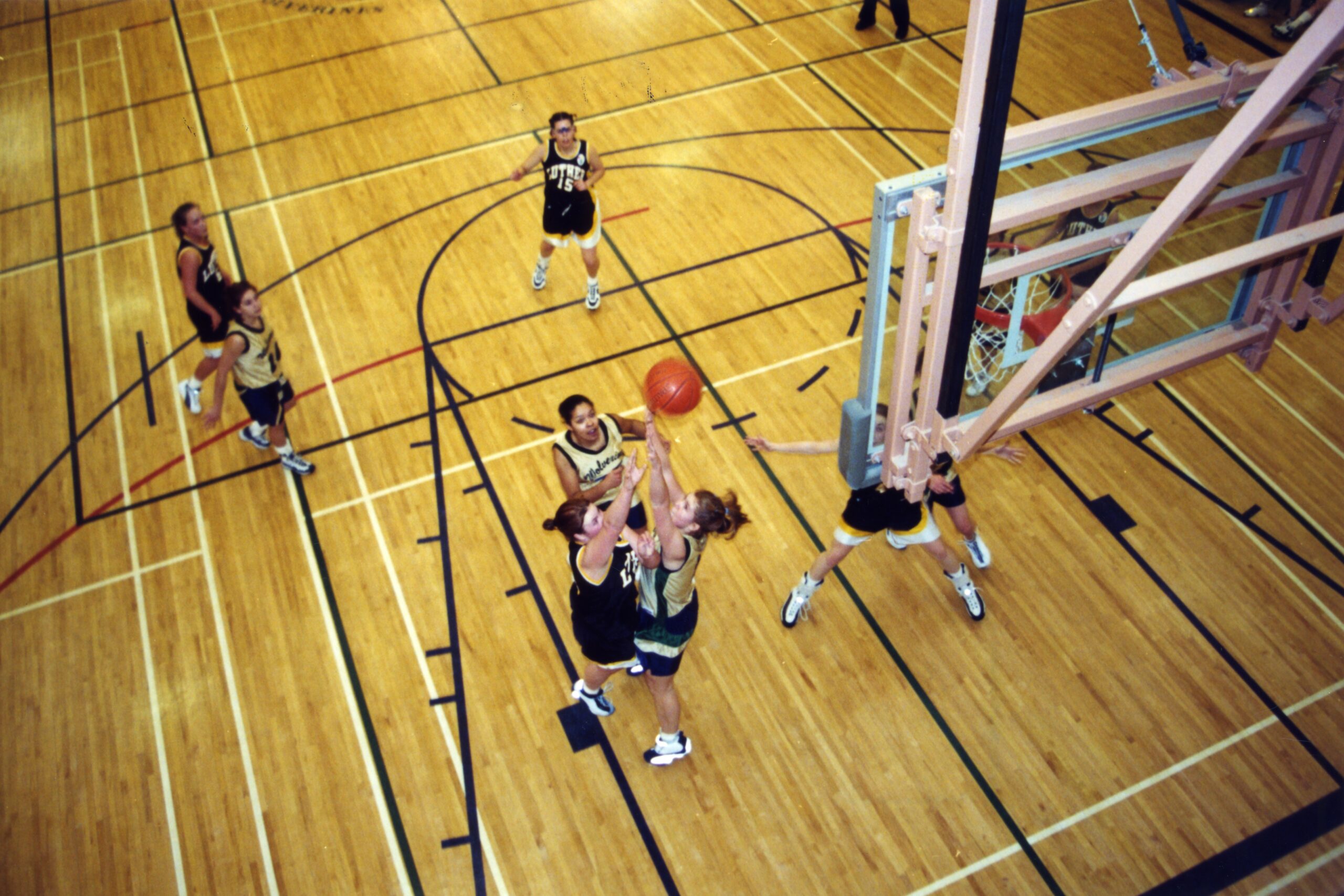 sports-girls-basketball-game-2001 High School Basketball Game: Exciting action during a high school basketball game with players in green and yellow uniforms. The packed gymnasium is filled with enthusiastic fans cheering from the bleachers. Colorful artwork and banners adorn the walls, enhancing the energetic atmosphere.
